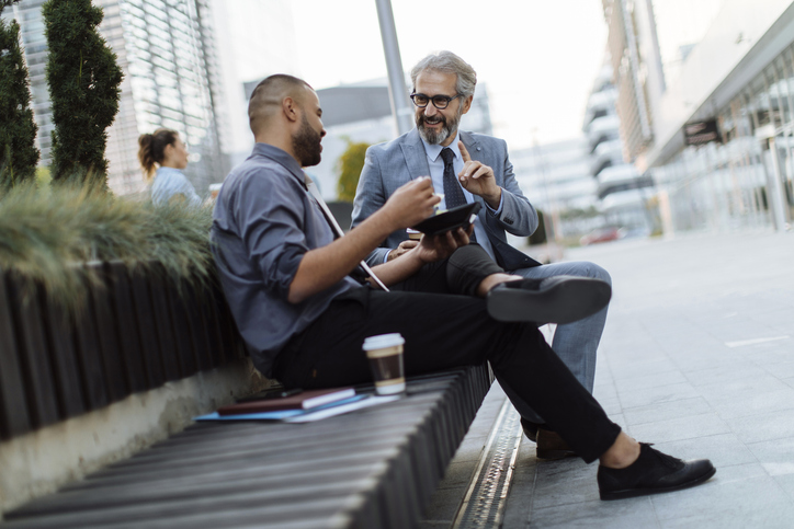 Two coworkers discussing work over lunch outside their office building while on a break